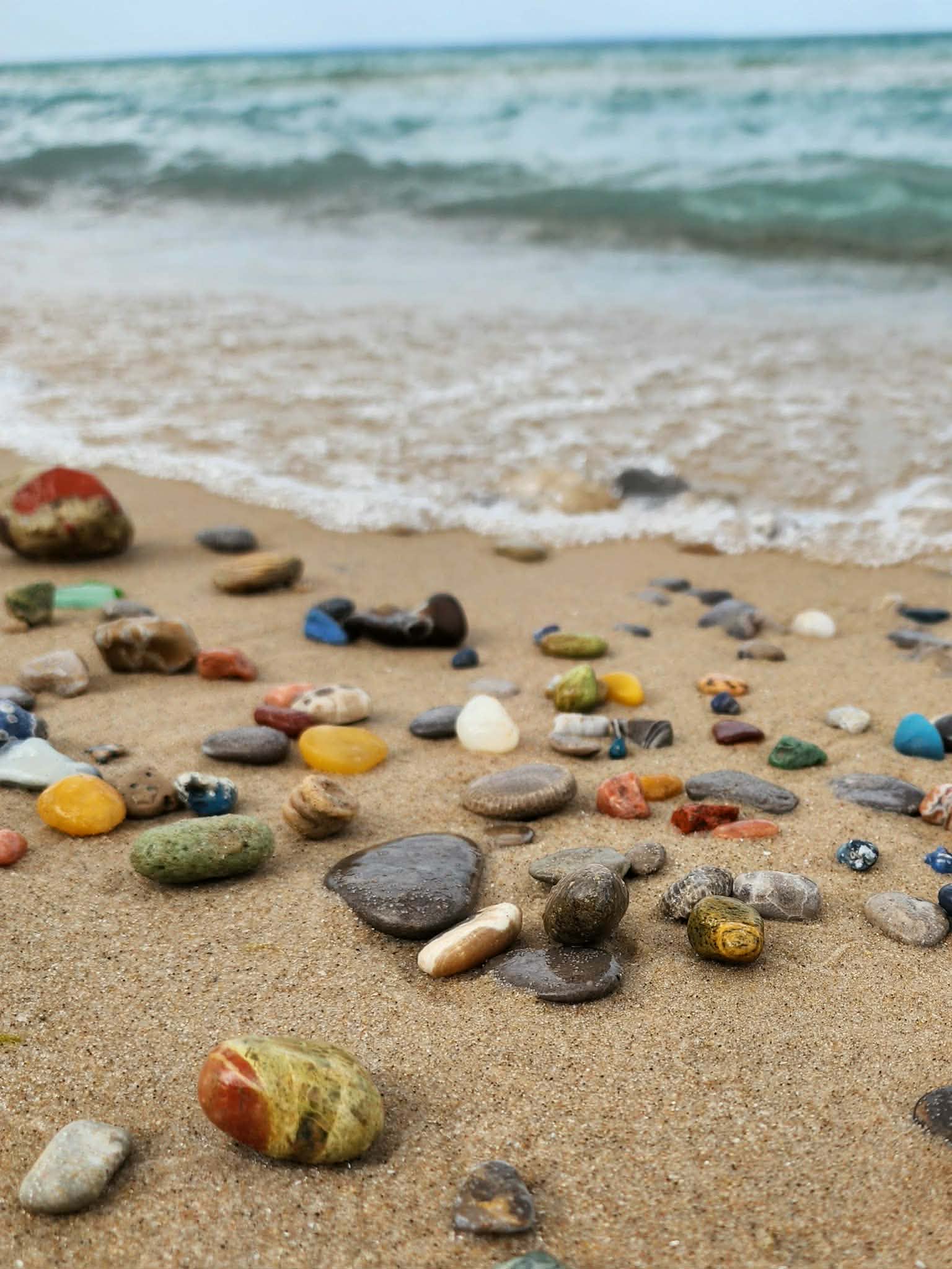 Colorful Michigan stones arranged on a sandy Lake Michigan shoreline